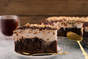 Sliced chocolate cake. White and brown layer. Sprinkle with ground nuts. Dishes for dessert. Wooden background.