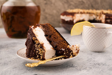 Delicious chocolate cake on a plate. Lemon on the Cup of tea. Light background. A pitcher of drink made from herbs.