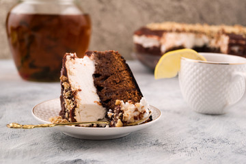 Piece of cake in a plate on the side. Brown and white layer. Spoon and pie. Eating dessert. Cup with slice of lemon. Light background.