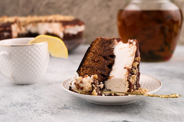 A piece of chocolate cake with a white layer. Lemon crowbar on the edge of the Cup. Pitcher of drink. Light background.