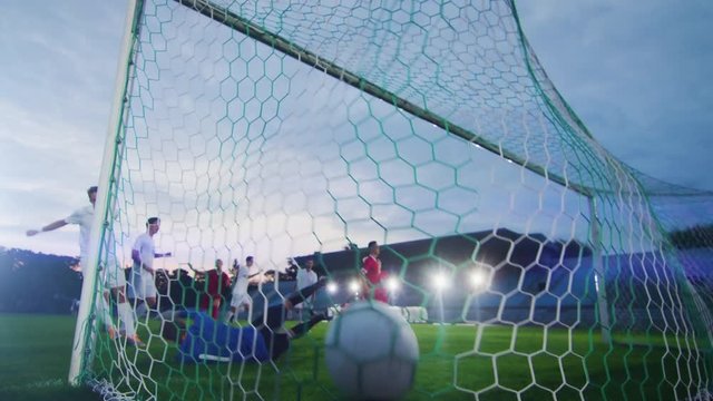 On Soccer Championship Player Kicks the Ball and Goalkeeper Tries to Defend Goals but Jumps and Fails to Catch the Ball. Camera Shot from Behind the Net with whole Stadium Visible.