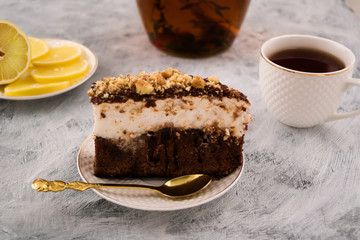 Delicious dessert of chocolate dough. Layer of white cream. The powder of grated nut. Tableware for cake. Light background.