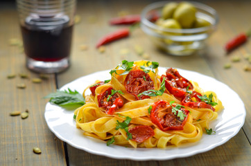 Spaghetti with grilled tomatoes and herbs. Mediterranean lunch with red wine. Wooden table with olives and hot red pepper.