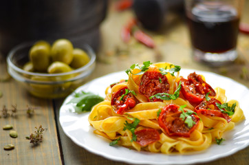 Spaghetti with grilled tomatoes and herbs. Mediterranean lunch with red wine. Wooden table with olives and hot red pepper.