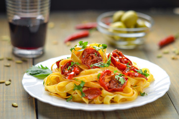 Spaghetti with grilled tomatoes and herbs. Mediterranean lunch with red wine. Wooden table with olives and hot red pepper.