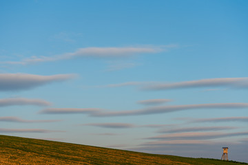 Jagdhochstand am Hügel mit sanfter Wolkenformation bei Sonnenuntergang