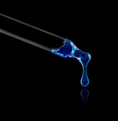 Blue liquid drop from cosmetic pipette close up on black background