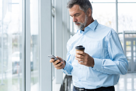 Mature business man in formal clothing using mobile phone. Serious businessman using smartphone at work. Manager in suit using cellphone in a modern office.