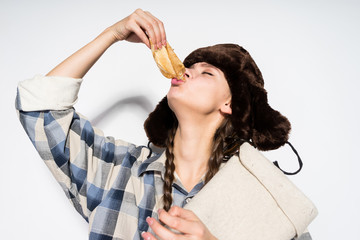 hungry Russian girl in a black hat eagerly eats hot pancakes, celebrates Shrovetide