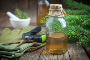 Fir aromatic oil. Pine essential oil in a glass bottle. Coniferous tree branches, gloves, pruner and mortar on background.