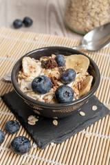 Yogurt with granola and fresh blueberries, in a ceramic black bowl on an old wood background.