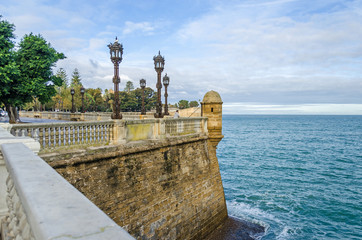 City walls with the park of Alameda Apodaca and a man fishing in the Old Town of Cadiz, Spain
