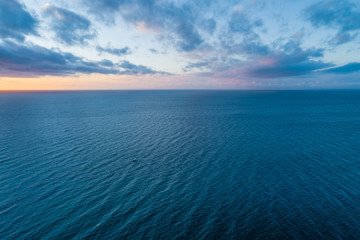 Tranquil seascape - clouds over calm water and tiny lonely boat at dusk