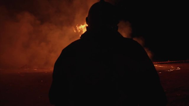 Pompier muni d'un jet d'eau se tient devant un feu 