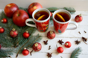 Obraz na płótnie Canvas Rozgrzewająca świąteczna herbata w czerwonych kubkach otoczona gałązkami świerku czerwonymi bombakmi i jabłkami