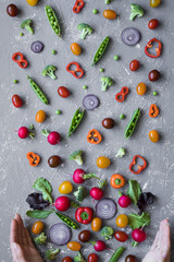 Clean eating concept. Fresh organic vegetables with hands. Radish, green peas, broccoli, tomato and onion on grey background. 