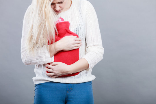 Woman feeling stomach cramps holding hot water bottle