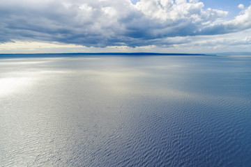 Small patch of land on the horizon with clouds over water - aerial landscape