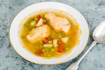 Fish soup with vegetables and salmon in white plate on gray background