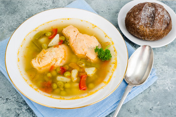 Fish soup with vegetables and salmon in white plate on gray background