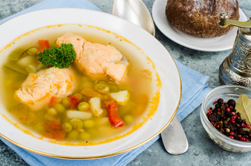 Fish soup with vegetables and salmon in white plate on gray background
