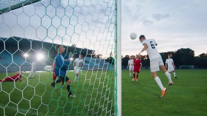 On Soccer Championship Player Scores the Goal Hitting Ball with His Head, Goalkeeper Tries to Defend Goals but Jumps and Fails to Catch the Ball. Camera Shot from Behind the Net with whole Stadium. - Powered by Adobe