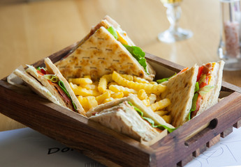 Four small sandwiches and french fries in a wooden plate on a table.