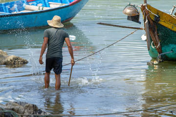 Man in water fishing with stick, surrounded by small colourful fishing boats, Vietnam