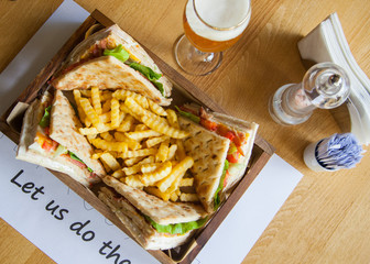 Four small sandwiches and french fries in a wooden plate on a table.