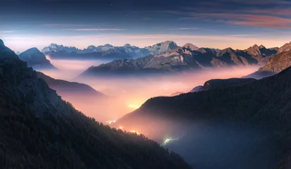 Peel and stick wall murals Living room Mountains in fog at beautiful night in autumn in Dolomites, Italy. Landscape with alpine mountain valley, low clouds, forest, colorful sky with stars, city illumination at dusk. Aerial. Passo Giau
