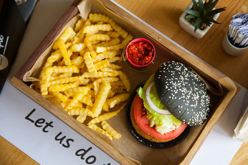 Black colored small mouth-watering, delicious burger on the wooden tray served with red ketchup sauce.