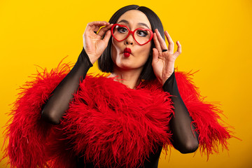 Asian woman with heart shaped glasses puckering her lips for a kiss with bright red lipstick