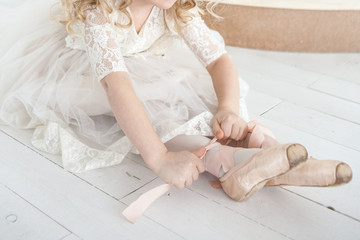 little ballerina in a white lush dress wears pointe shoes