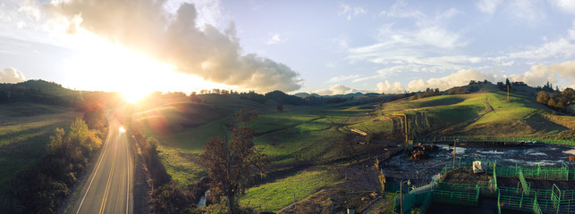 Aerial panorama of sunset over rolling hills and two lane road in country-side