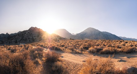 Sunset behind mountains in desert with fence and road in foreground