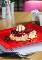 American pancake with ice cream, jam and berry served in a restourant on a red plate