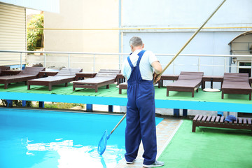 Male worker cleaning outdoor pool with scoop net