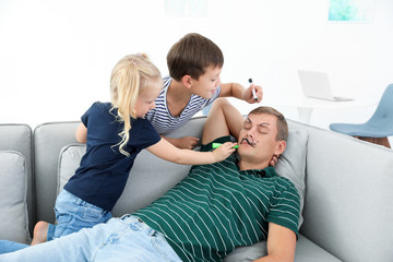 Little children painting their father's face while he sleeping on couch at home. April fool's day...