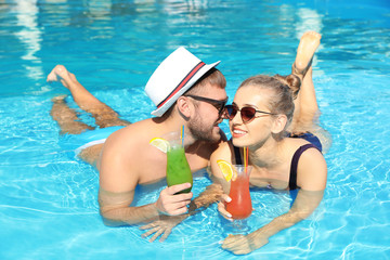 Young couple with refreshing cocktails in swimming pool at resort