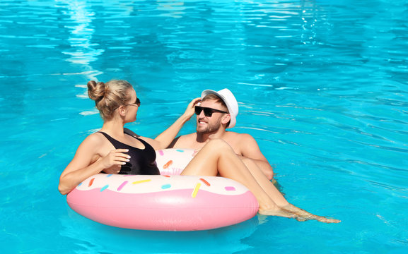 Happy young couple with inflatable ring in swimming pool - Powered by Adobe