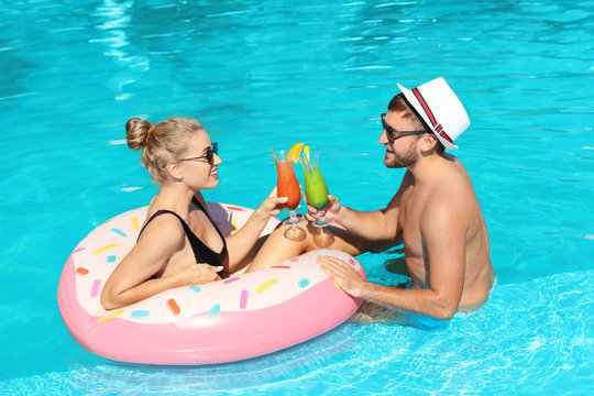 Young couple with refreshing cocktails and inflatable ring in swimming pool
