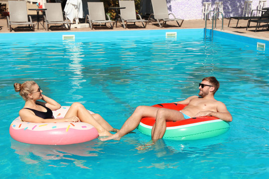 Happy young couple with inflatable rings in swimming pool