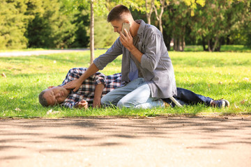 Passerby calling ambulance while checking pulse of unconscious man outdoors. First aid