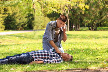 Passerby calling ambulance while checking pulse of unconscious man outdoors. First aid