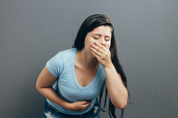 Portrait of young woman drunk or sick vomiting over gray background