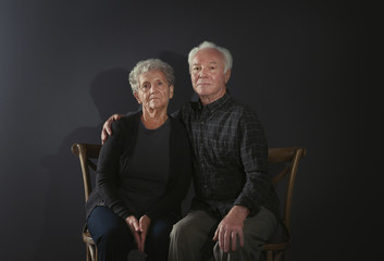 Portrait of poor elderly couple on dark background