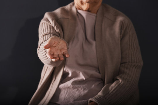 Poor elderly woman begging for money on dark background. Focus on hand