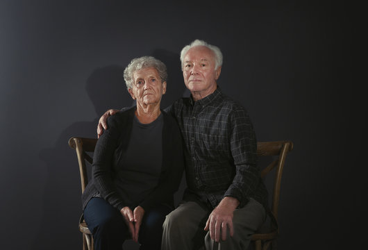 Portrait Of Poor Elderly Couple On Dark Background