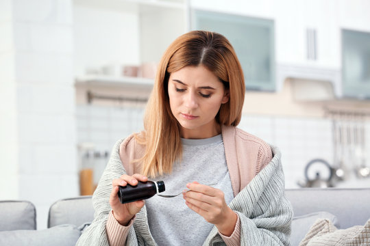 Woman Taking Cough Syrup On Sofa At Home