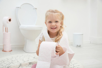 Cute little girl playing with toilet paper in bathroom
